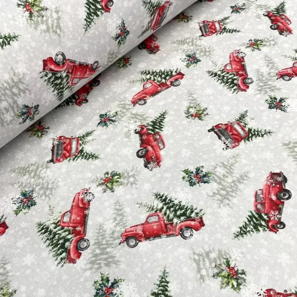 Tela navideña Arnold con camionetas rojas cargando pinos sobre fondo gris con nieve y acebo.