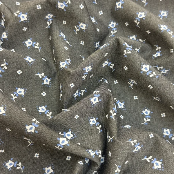 Polo Chambray Flores Celestes con pequeñas flores azules y blancas estampadas sobre fondo gris para confección de prendas.