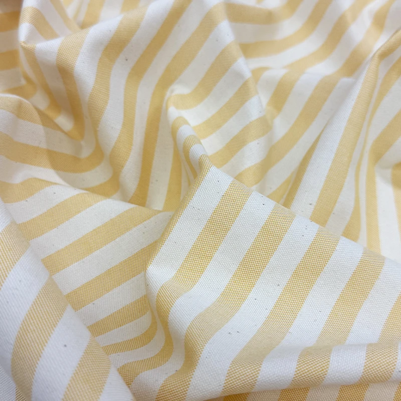 Tela decorativa Raya Mango con diseño de franjas color mango sobre fondo crudo, ideal para cortinas, mantelería y decoración del hogar.