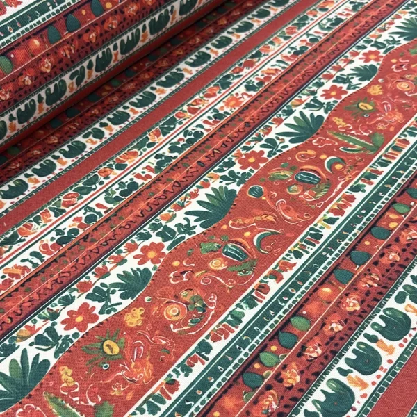 Tela mantelera Caminos de Oaxaca con franjas decorativas, flores y motivos artesanales en tonos terracota, verde y blanco.