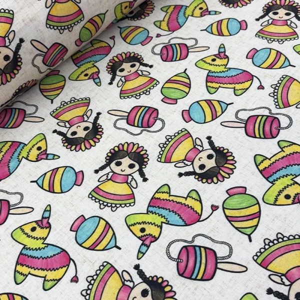 Tela mantelera Feria de Colores con estampado de muñequitas mexicanas, piñatas, trompos y baleros sobre fondo color crudo.
