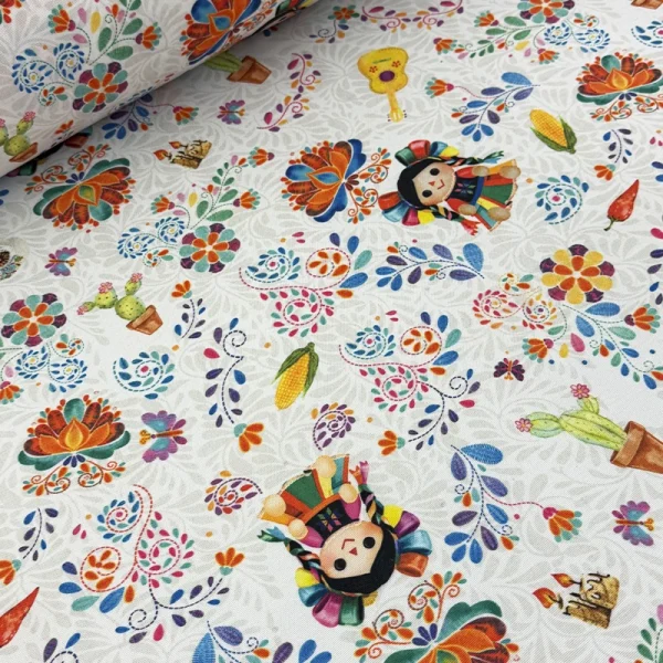 Tela mantelera Fiesta Artesanal con estampado de muñecas mexicanas, flores, guitarras, maíz y nopales sobre fondo blanco.