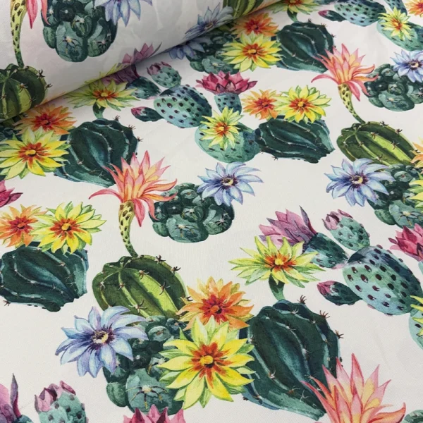 Tela mantelera Jardín del Desierto con estampado de cactus verdes y flores de colores sobre fondo blanco.